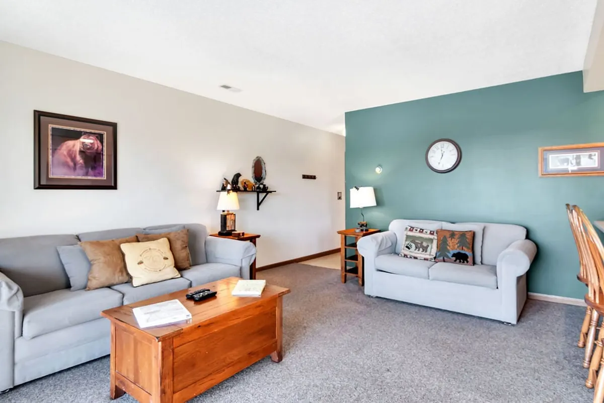 A warm, inviting living room with plush sofas and a wooden coffee table, accented by tasteful wall art and a green feature wall. The arrangement encourages relaxation, conversation, and game nights, reflecting the room's role as a gathering space.