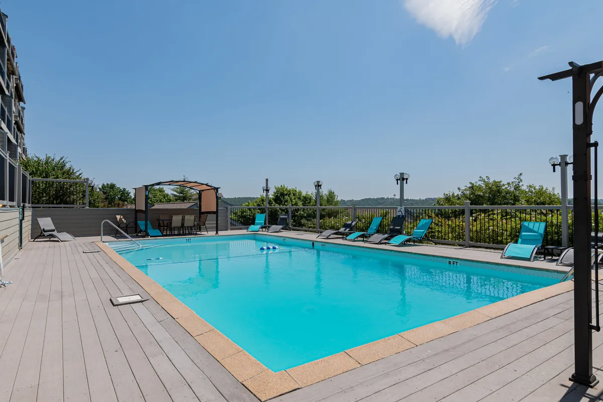 This image showcases a lively outdoor pool scene surrounded by lounge chairs, a canopy structure, and lush landscaped greenery. The mood is leisurely and inviting, with visible enjoyment of the pool and relaxation spaces, enhanced by the warm glow of a sunset.