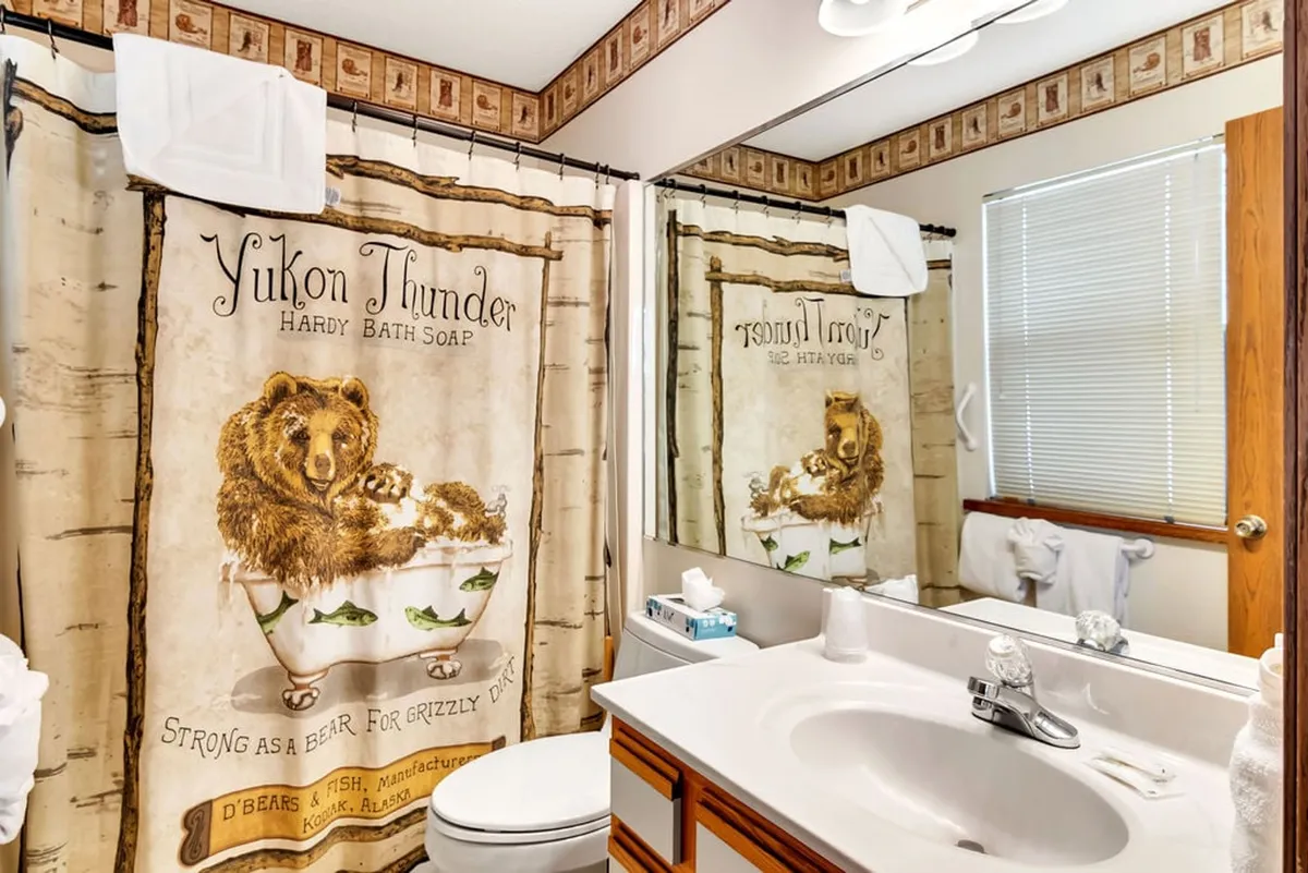 A bathroom featuring a whimsical bear-themed shower curtain, a mirror reflecting the room, a bathroom sink, and a spacious countertop. The decor is playful yet practical, and the space is well-lit—ideal for refreshing and recharging after a long day.