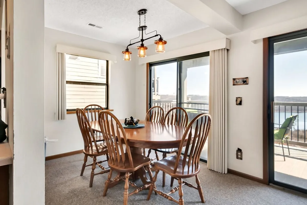 A welcoming dining area with a sturdy wooden table, matching chairs, and a modern light fixture. Large windows offer glimpses of the outdoors, creating a cozy spot for shared meals, family celebrations, or board games.