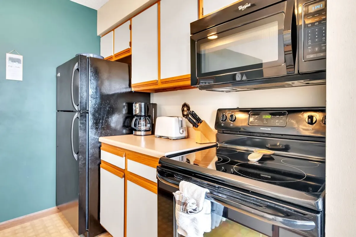 A well-equipped kitchen area with a black refrigerator, a coffee maker, a microwave, an oven, and a toaster. The appliances are modern, and the layout feels homey yet practical, ideal for families or long-term guests.