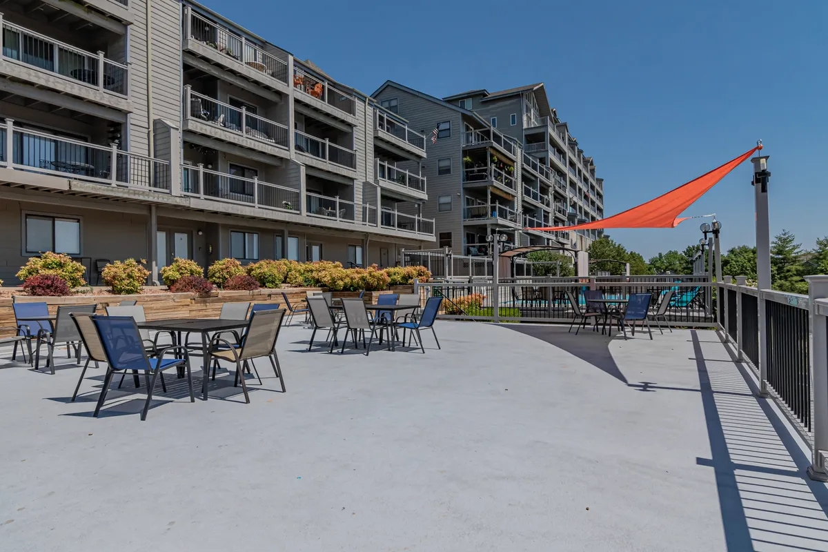 An inviting outdoor seating area with colorful umbrellas, flower beds, and a modern apartment building. The space is ideal for socializing, relaxing, or enjoying meals outdoors, with a cheerful and communal atmosphere.