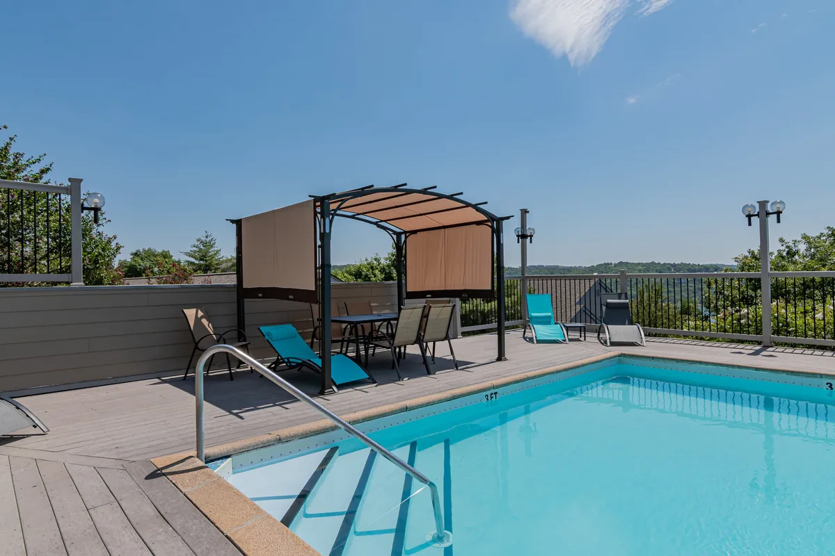 Another angle on the shared outdoor pool, this image highlights the inviting canopy seating area, lounge chairs, and a sweeping view of the landscape beyond the pool. The atmosphere is tranquil, ideal for both summer gatherings and quiet mornings.